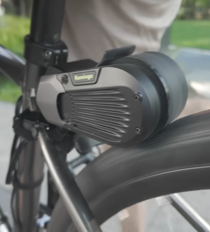 Close-up of a Kamingo friction drive unit attached to the rear wheel of a commuter bicycle with a city street in soft focus