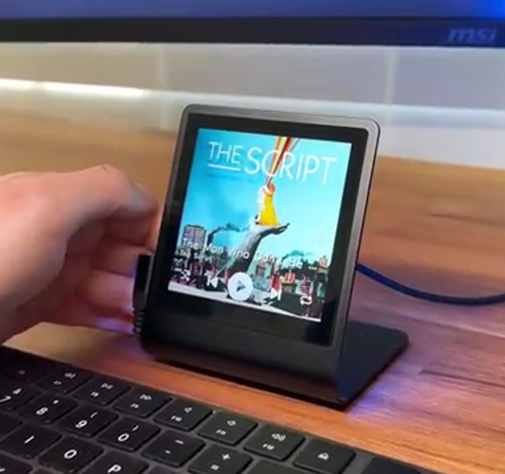Vertical photo of a Pimoroni Presto board mounted on a Raspberry Pi Pico configured as a compact Spotify desk player, showing the OLED display and rotary encoder on a wooden desk