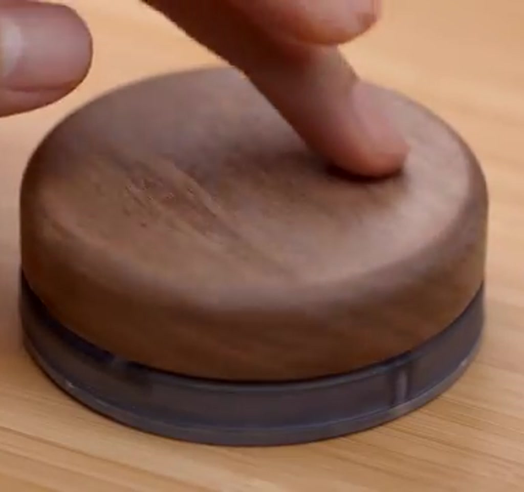 Vertical view showing a hand rotating a machined knob mounted to a compact PCB beside a laptop and USB cable